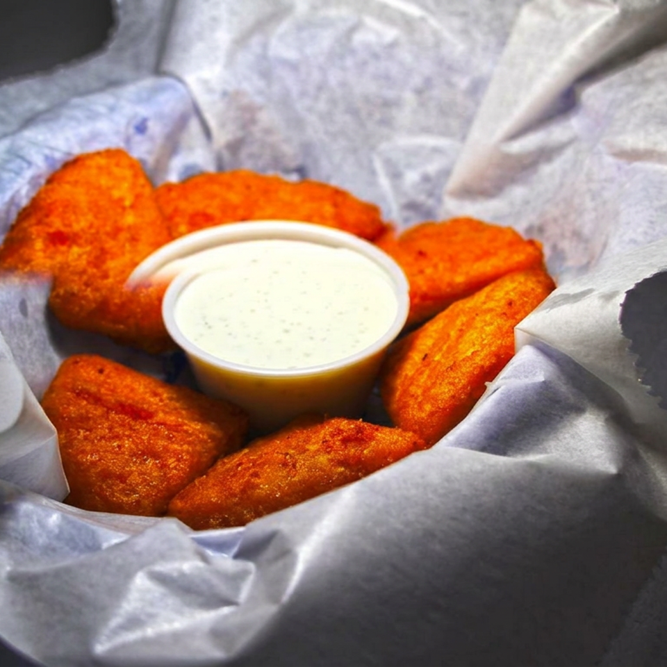 Basket of golden-brown fried wings surrounding a cup of creamy dipping sauce on parchment paper.